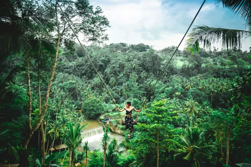 young woman sitting at the bali swing with green forest in the background